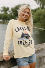 Woman wearing a 'Lake Life Forever' sweatshirt standing on a wooden bridge by a lake.