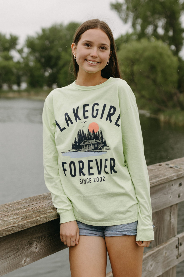 Person wearing a 'Lakegirl Forever' sweatshirt standing on a wooden dock by a lake.