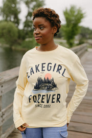 Person wearing a 'Lakegirl Forever' sweatshirt standing on a wooden bridge by a lake.