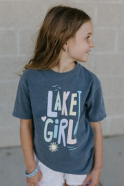 Young girl wearing a 'Lake Girl' t-shirt against a brick wall.