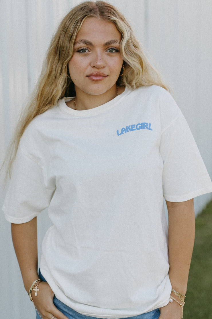 Woman wearing a white t-shirt with text, standing against a light-colored wall.