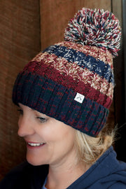 Person wearing a colorful striped beanie with a pom-pom against a wooden background