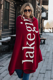 Woman wearing a red 'Lakegirl' blaon a wooden deck with snowy landscape.