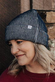 Woman wearing a ribbed beanie and red sweater against a stone wall.
