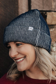 Woman wearing a ribbed beanie and red sweatshirt standing against a stone wall.