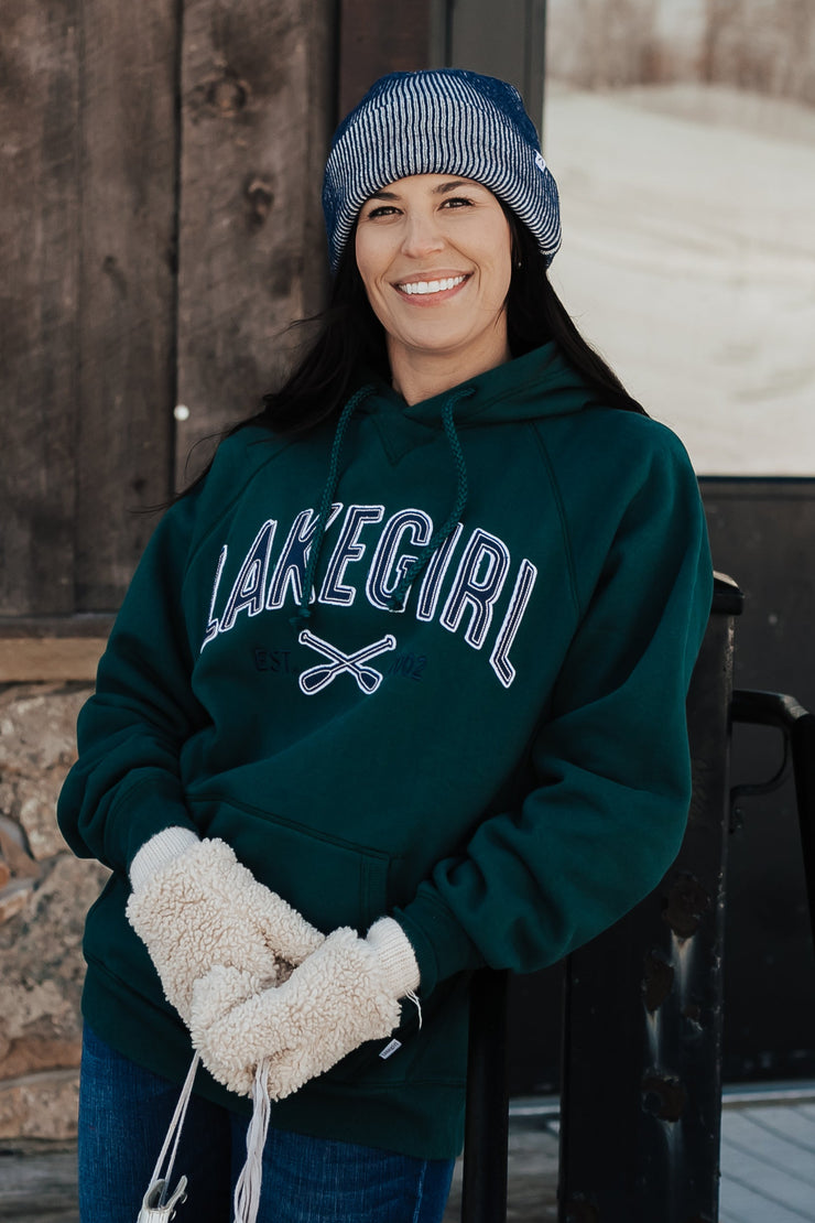 Person wearing a green sweatshirt with 'Lakegal' text, standing outdoors in front of a wooden building.