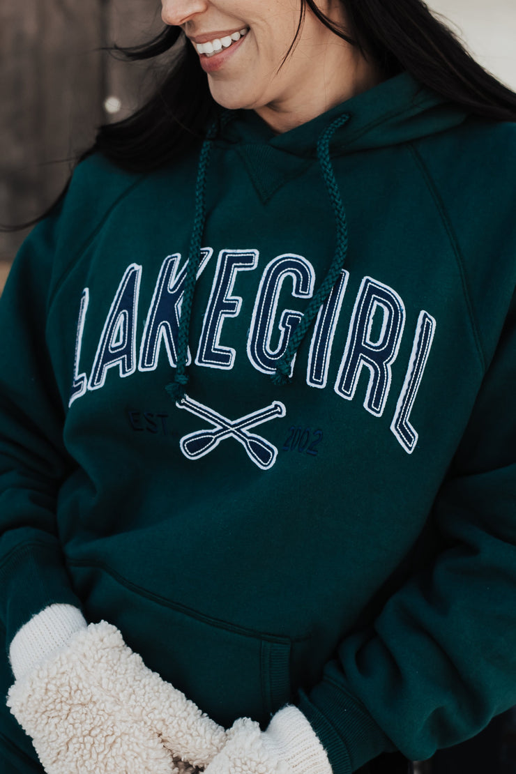 Person wearing a green 'Lake Girl' hoodie with a wooden cabin background