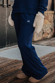Person wearing navy blue pants with a logo, standing on a wooden deck.