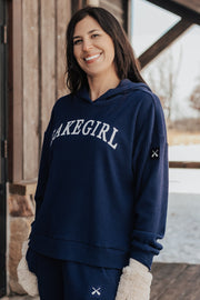 Woman wearing a navy blue sweatshirt with 'Lakegirl' text, standing on a wooden deck with a snowy landscape in the background.
