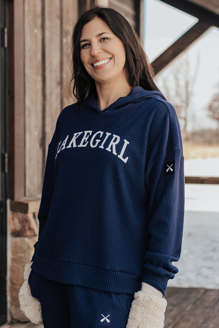 Woman wearing a navy blue sweatshirt with 'Lakegirl' text, standing on a wooden deck with a snowy landscape in the background.