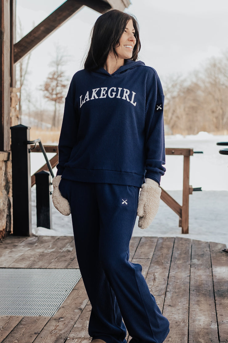 Woman wearing a navy sweatshirt with 'MAKEGIRL' text on a wooden deck in a snowy landscape.
