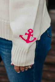 Beige sweater with pink anchor design worn by a person, blurred background