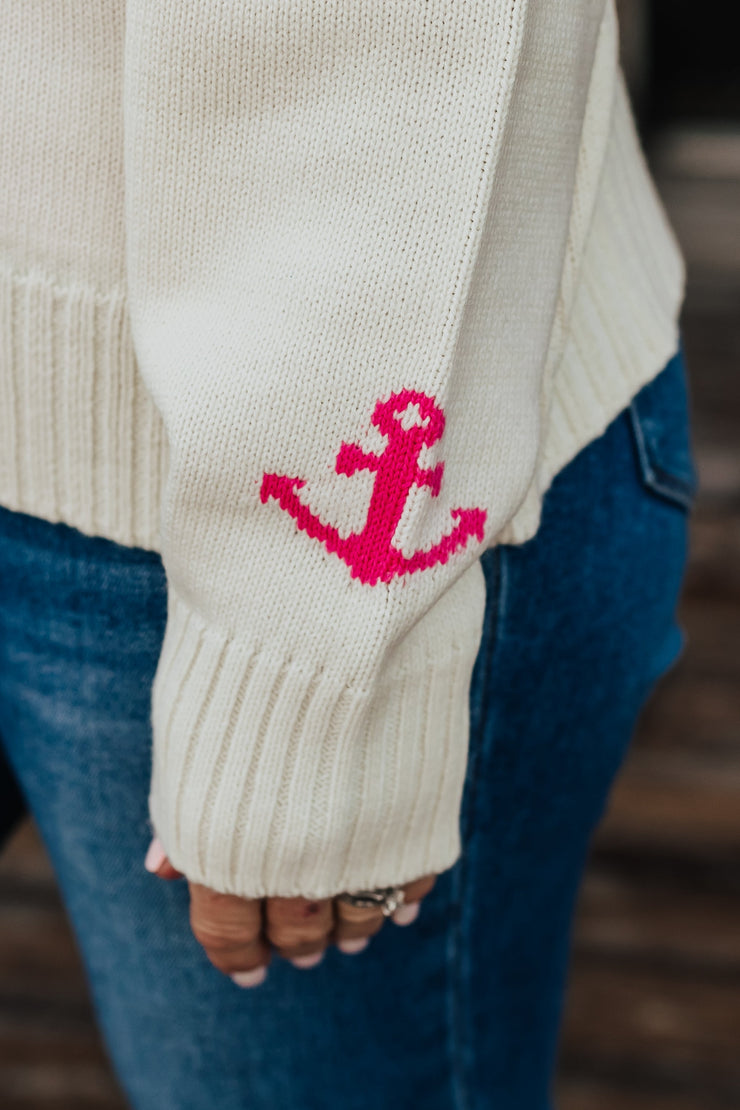 Beige sweater with pink anchor design worn by a person, blurred background