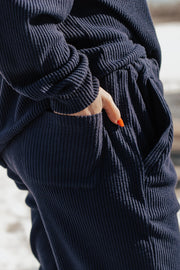 Person wearing a navy blue ribbed tracksuit with blurred background