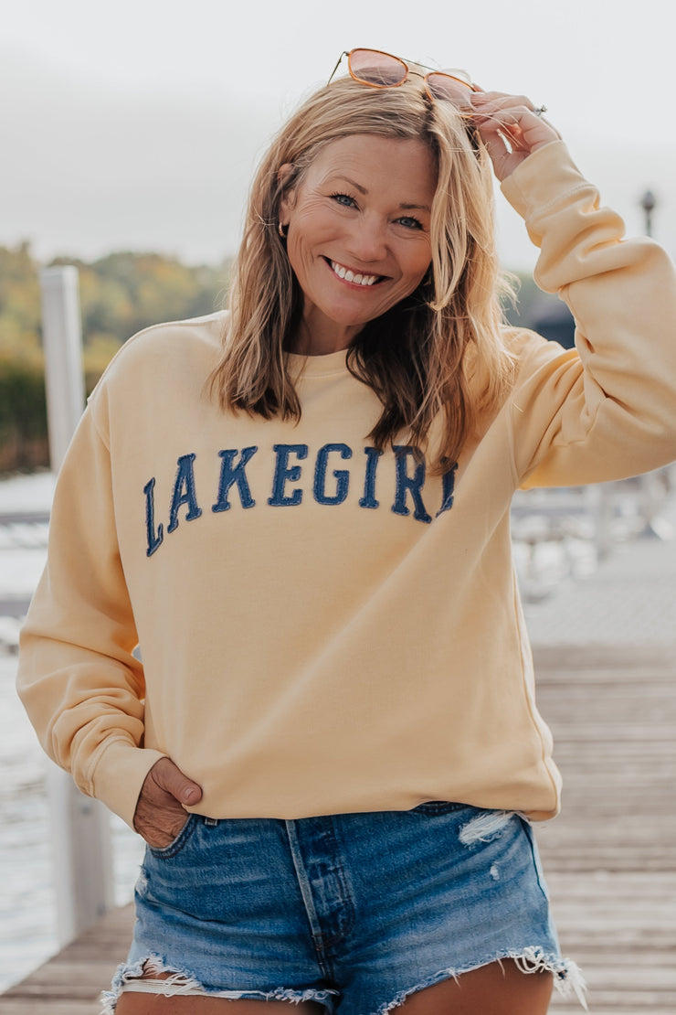Woman wearing a 'Lakegirl' sweatshirt on a wooden dock by a lake.