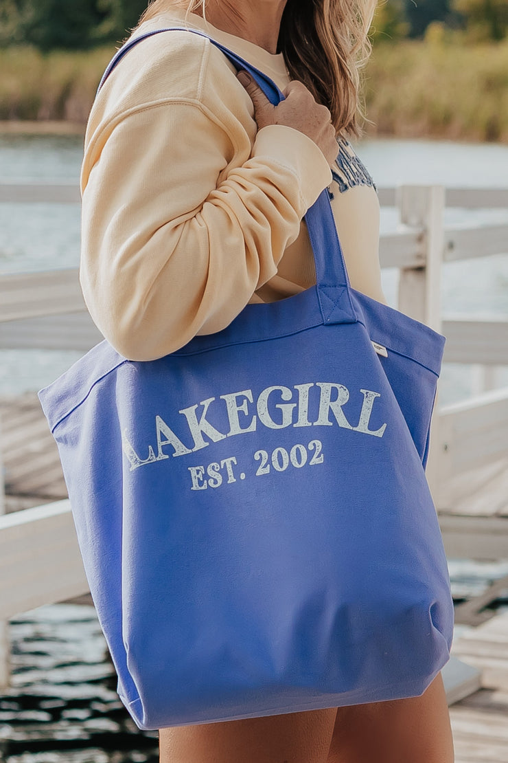 Woman holding a peri tote bag with 'LakeGirl' text by a lake