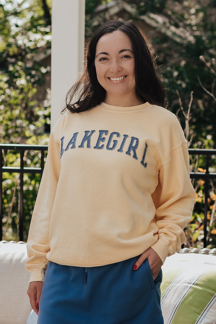 Woman wearing a 'Lakegirl' sweatshirt standing outdoors with a couch and plants in the background
